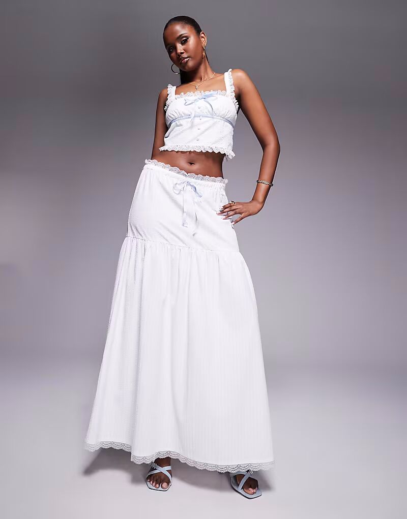 

Эксклюзивная юбка макси белого цвета с заниженной талией, отделкой из фактурного кружева и синими завязками Kaiia