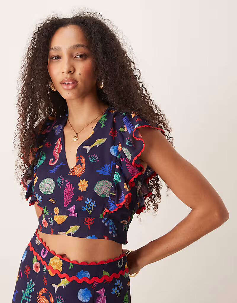 

Укороченный топ с оборками на рукавах и завязками на спине, с принтом ракушек в тёмно-синем цвете Hope & Ivy